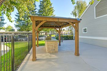 A wooden pergola with a stone pillar in the middle of a concrete walkway.